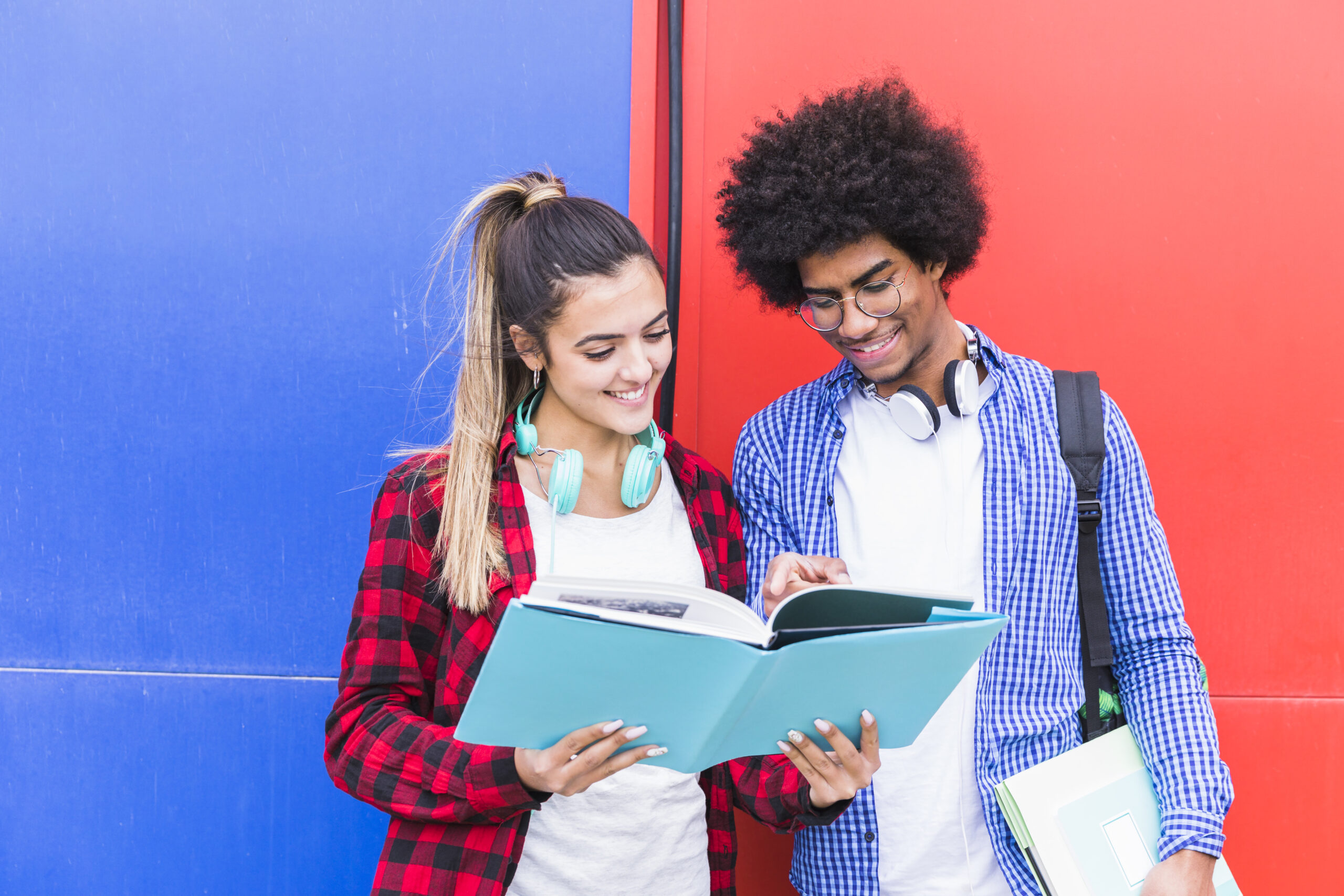 portrait happy young couple studying together standing against red blue wall