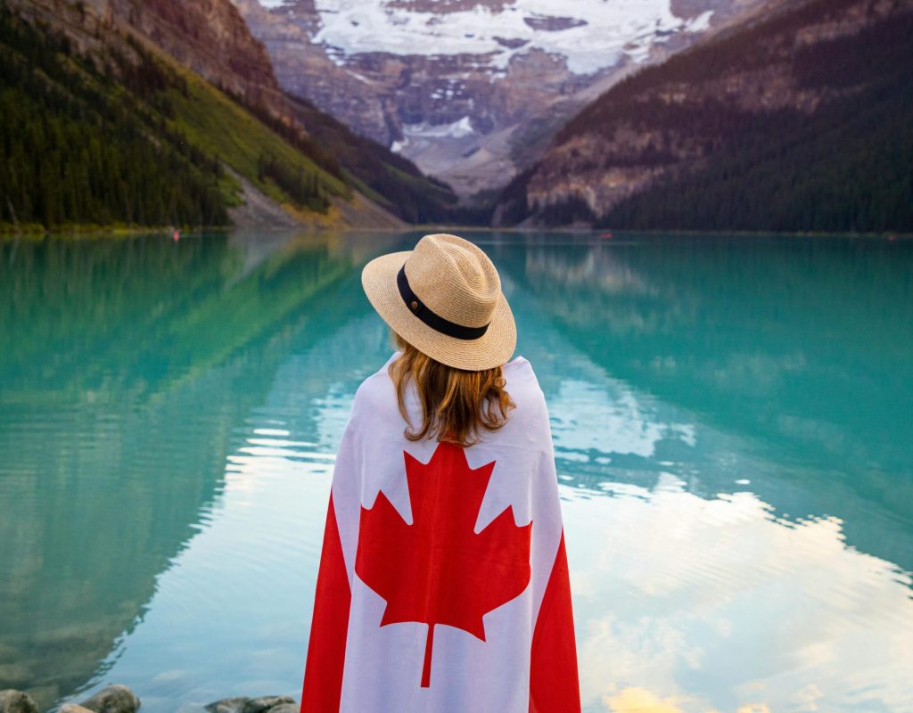 Woman in sun hat with Canadian flag enjoying tranquil Lake Louise, Alberta.