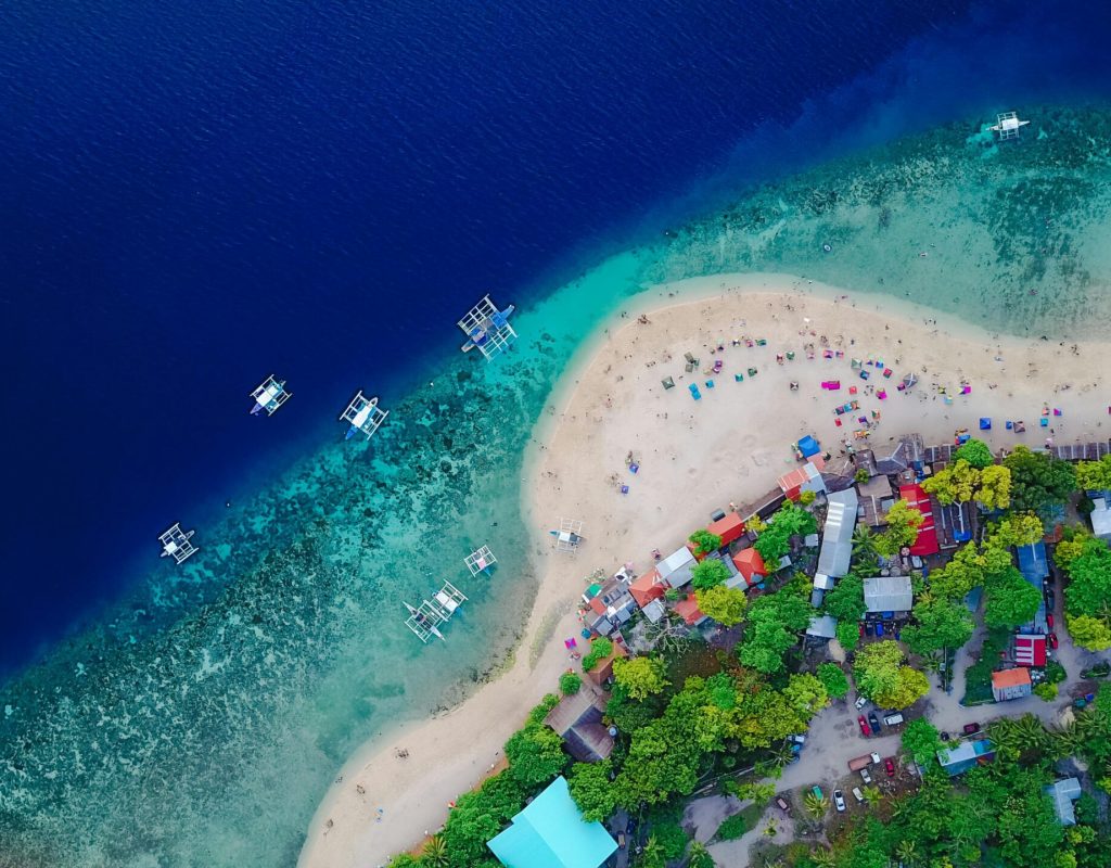 A stunning aerial view of Oslob Beach, Cebu, with vibrant blue waters and lush greenery.